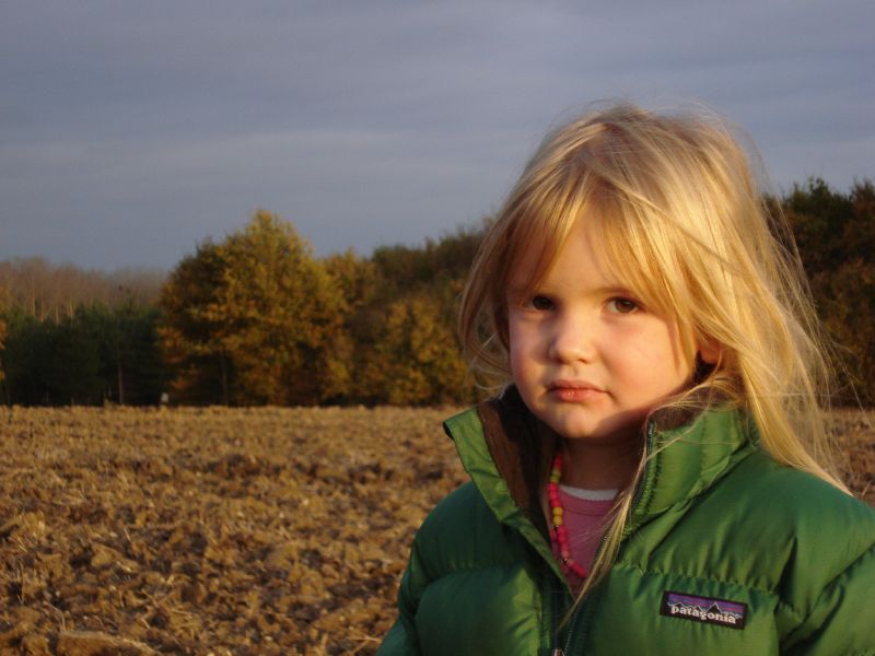 a blonde haired girl in green jacket next to a tree