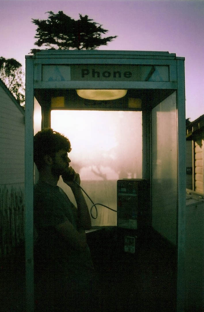 the person is using his phone at the telephone booth