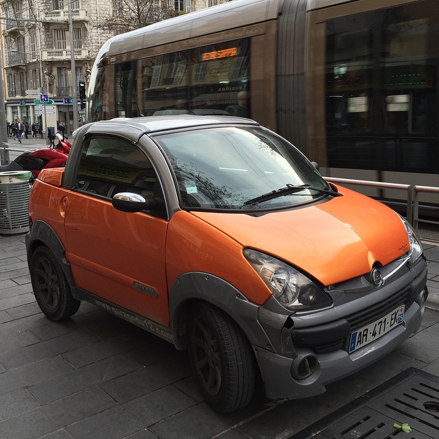 an orange car sits parked beside a busy street