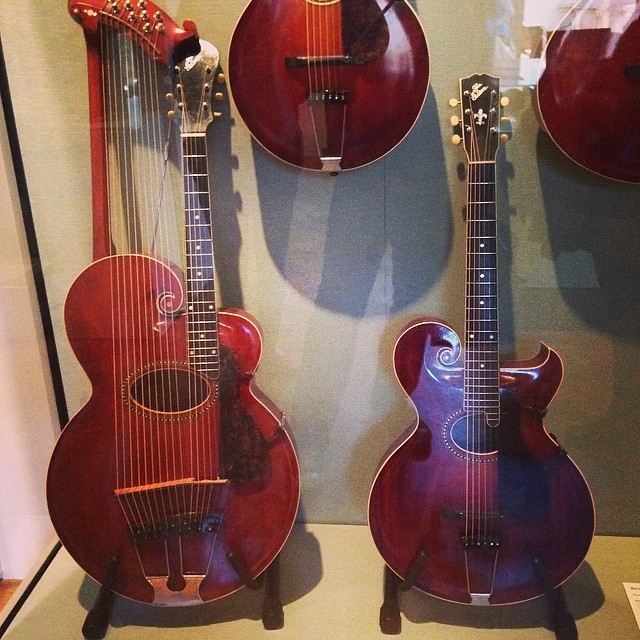 two guitars and an instrument on display in a glass case