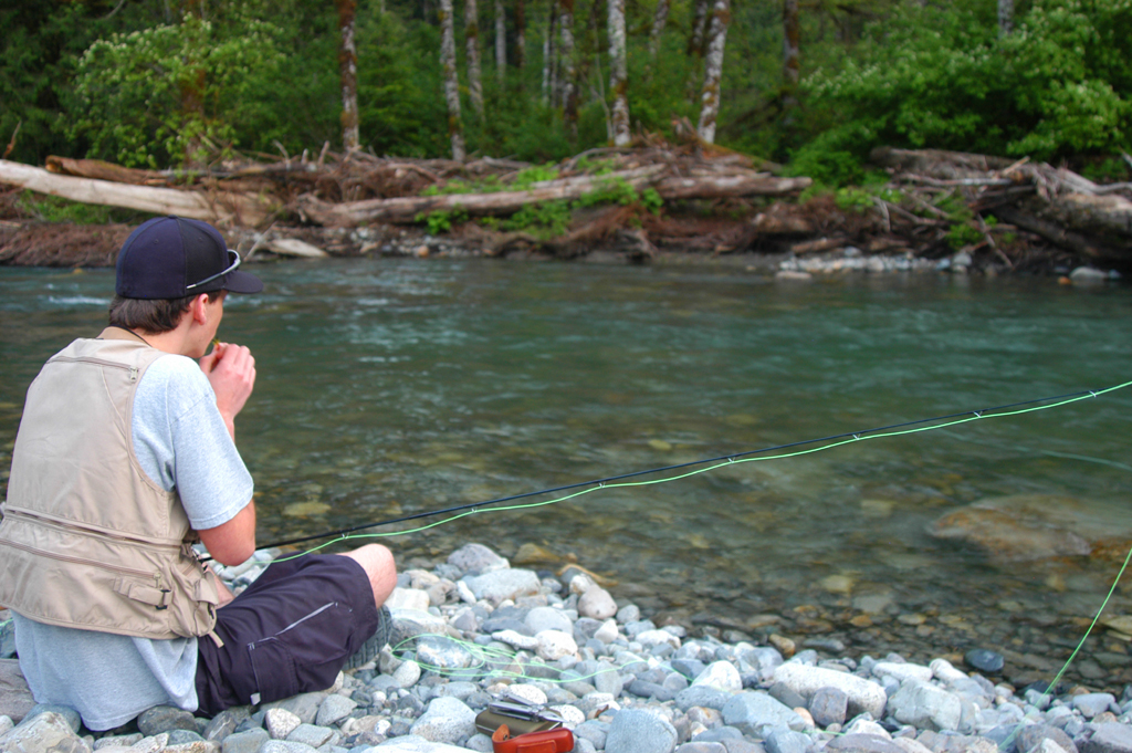 a man is sitting on rocks by the river with a fishing rod