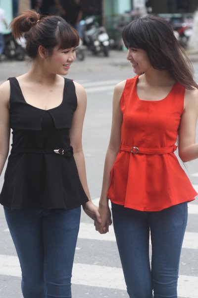 two woman walk along the side of a street with a motorcycle in the background