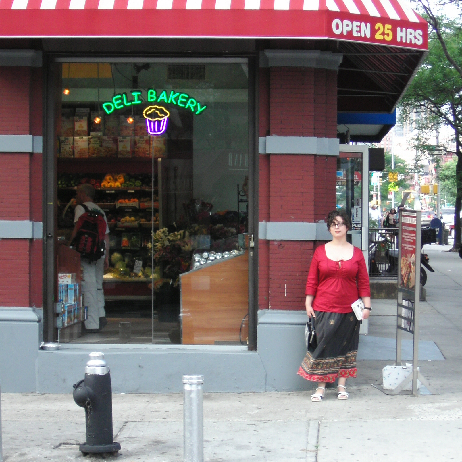 a woman standing outside of a deli bakery holding a shopping bag