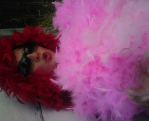 a woman in red feathers and pink wig laying down