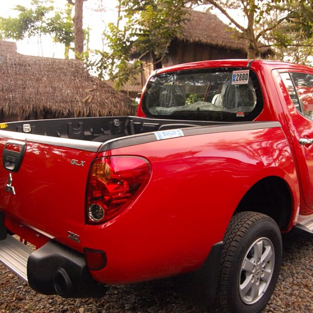 a red truck with its top open sitting in gravel next to trees