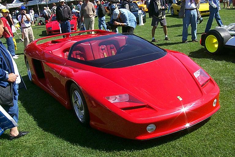 a red ferrari on display on the grass in front of a large group of people