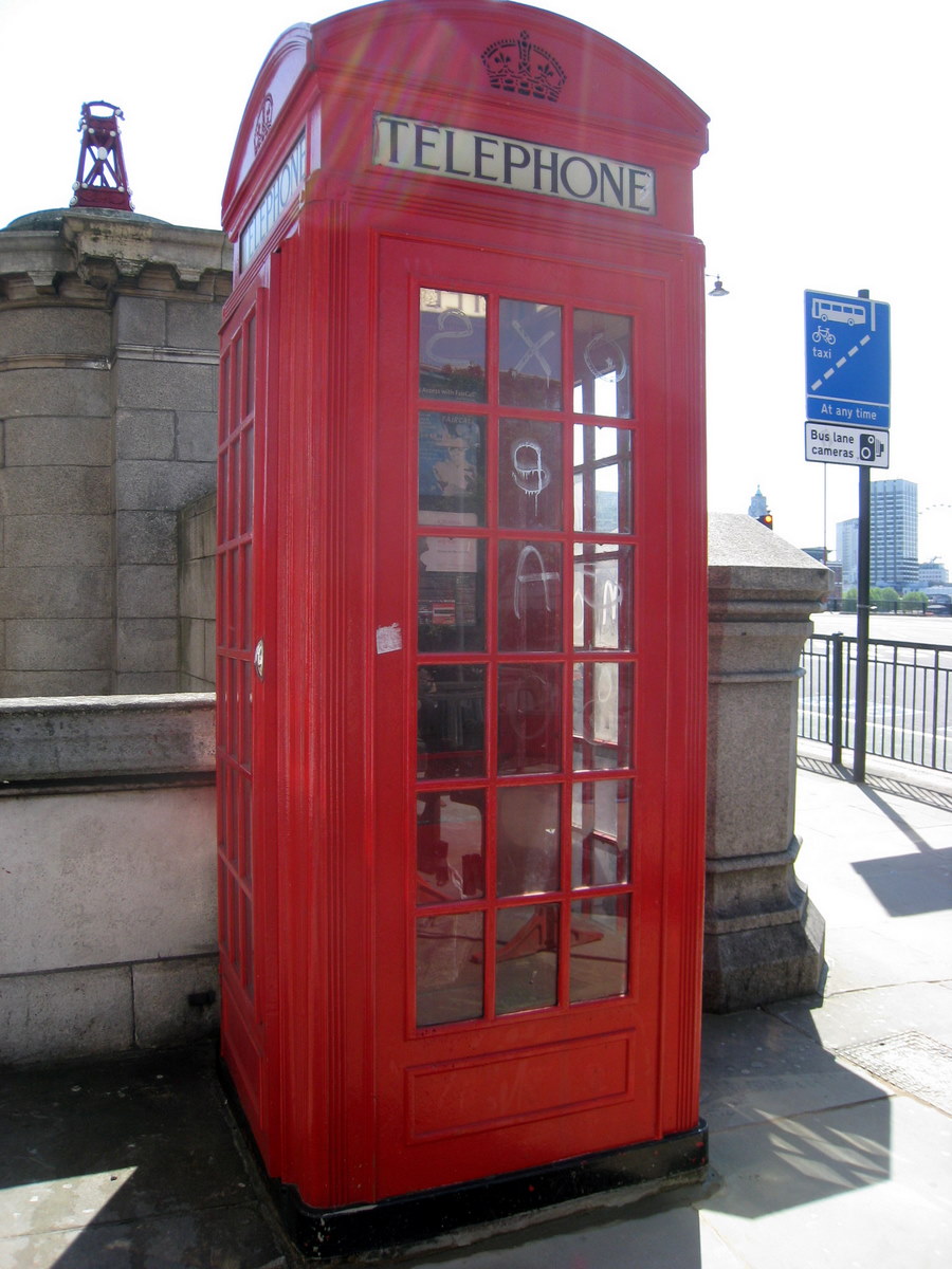 a red phone booth sits by the sidewalk