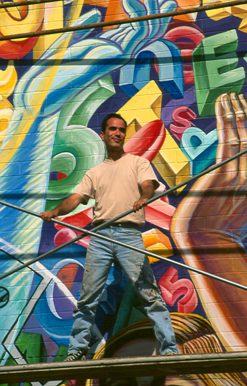 man standing on a metal hand rail next to a wall painted with images and shapes