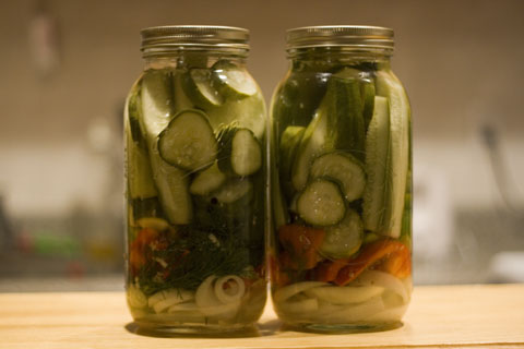 there are two jars with sliced cucumbers and herbs inside