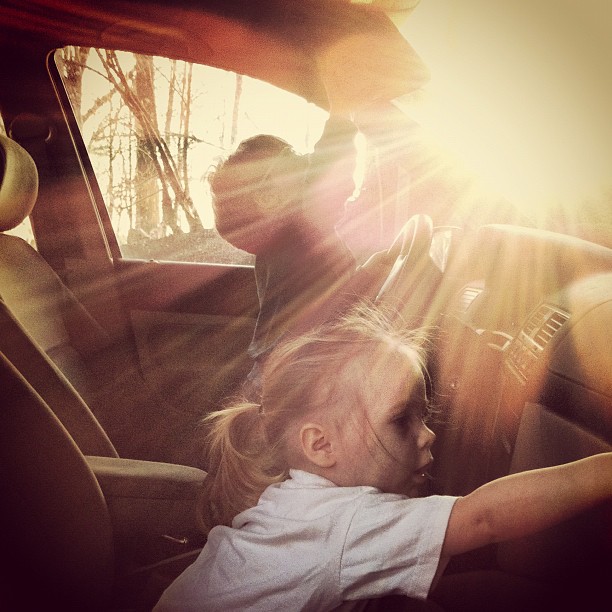 an older woman holds a child up in the back seat of a car