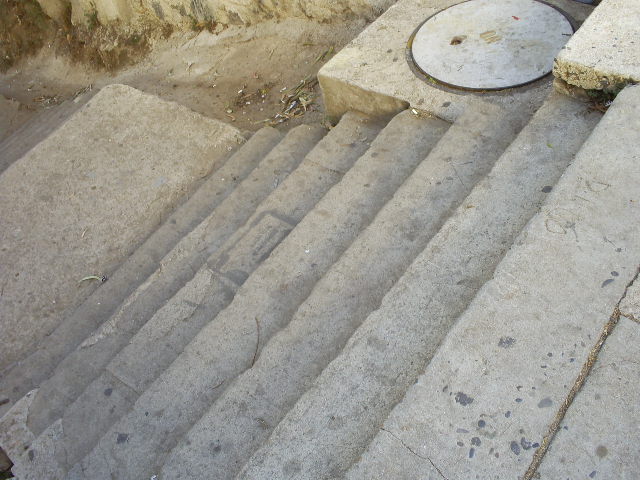 concrete steps going up into the dirt, near a rock