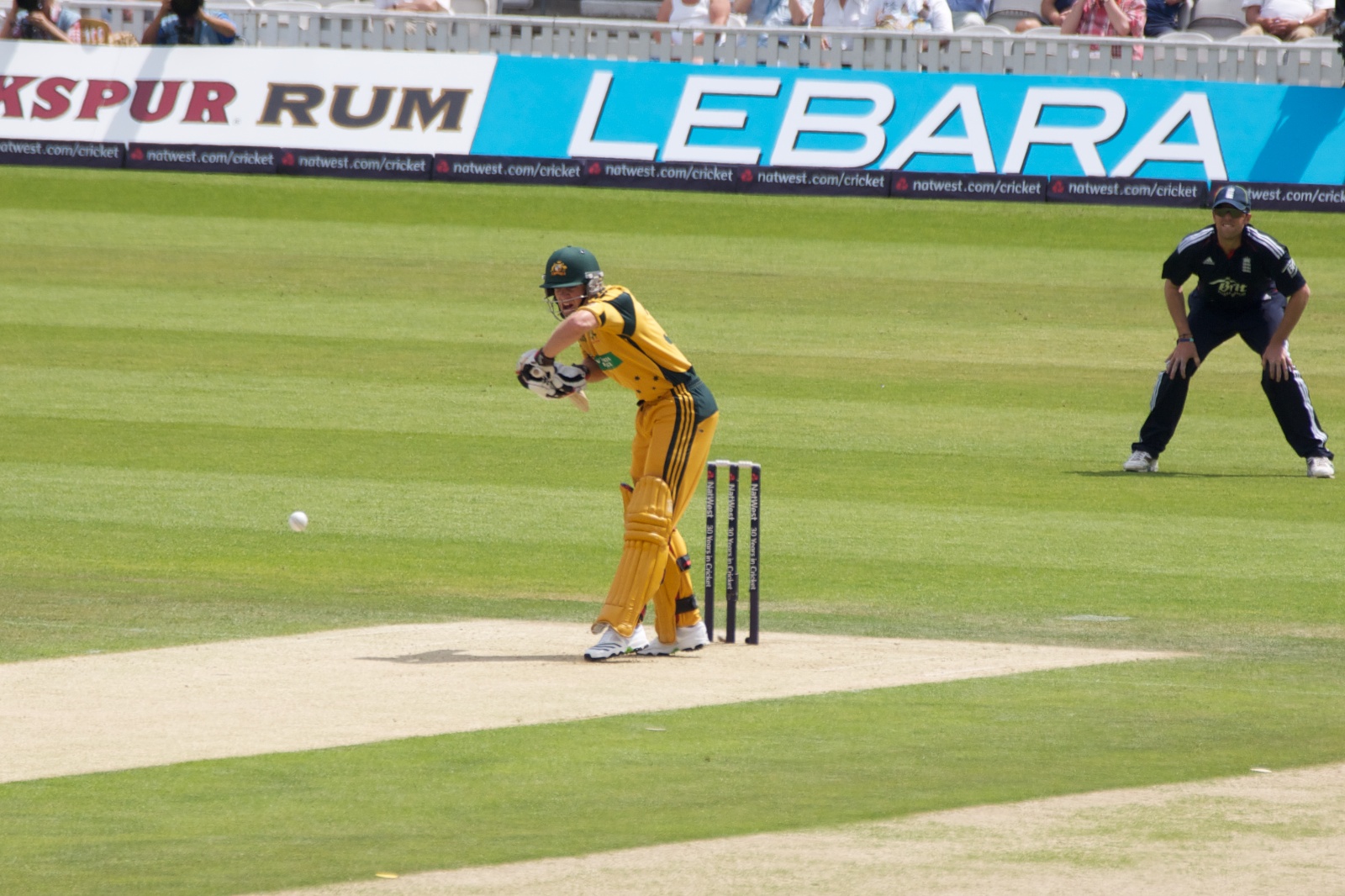 a man in an orange uniform and gloves playing cricket