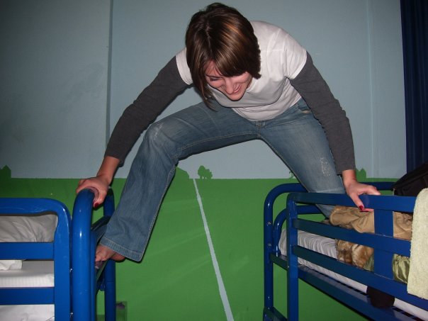 a woman climbs over the top of a bed in a room with bunk beds