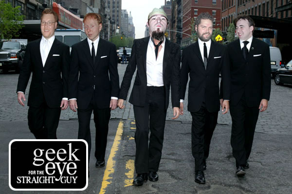 four men in suits walk down the street