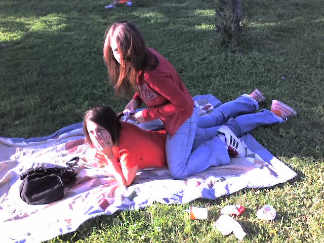 two women laying on the grass having drinks and eating