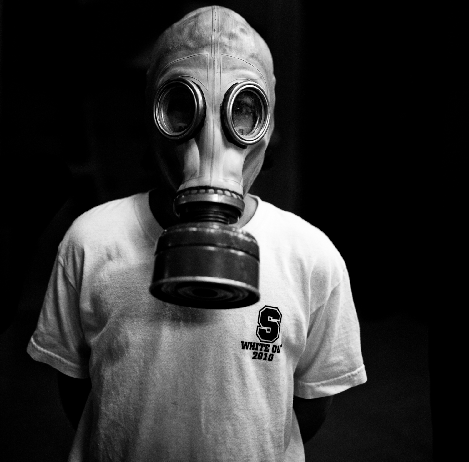 man wearing a gas mask stands against a black background