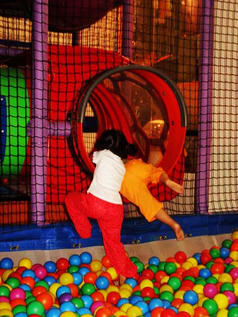 a little girl in an obstacle room climbing on a ball pit