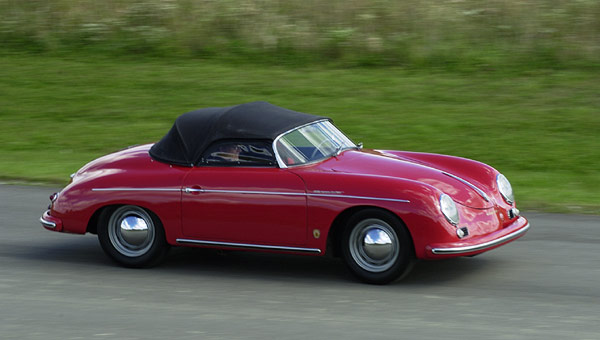 a red car with a black top driving down a road