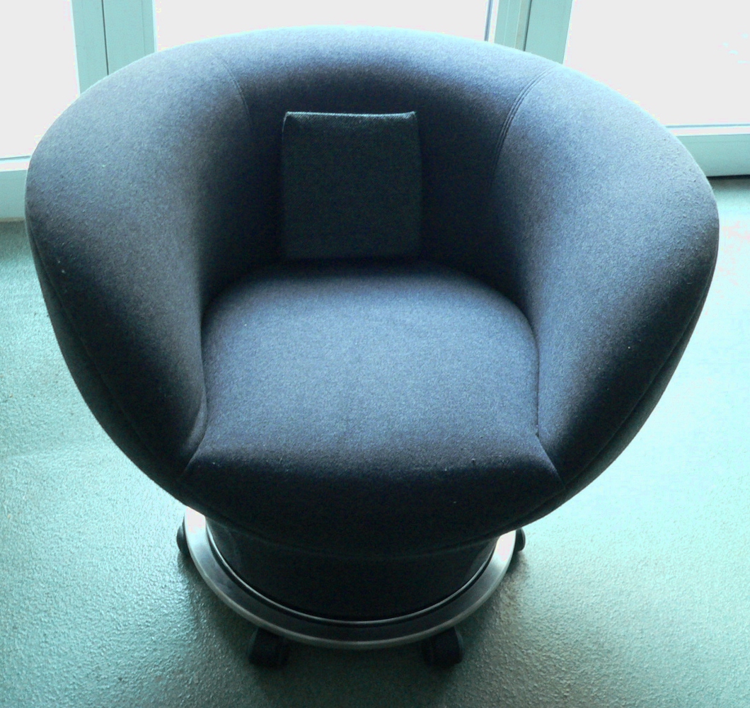 a black chair sits by a window on top of a circular pedestal
