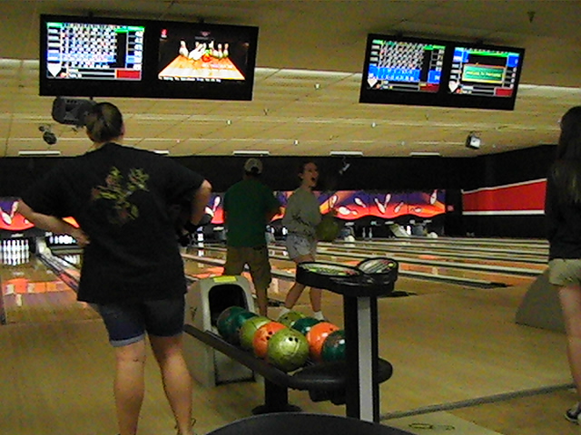 young adults at bowling alley playing bowling on television screens
