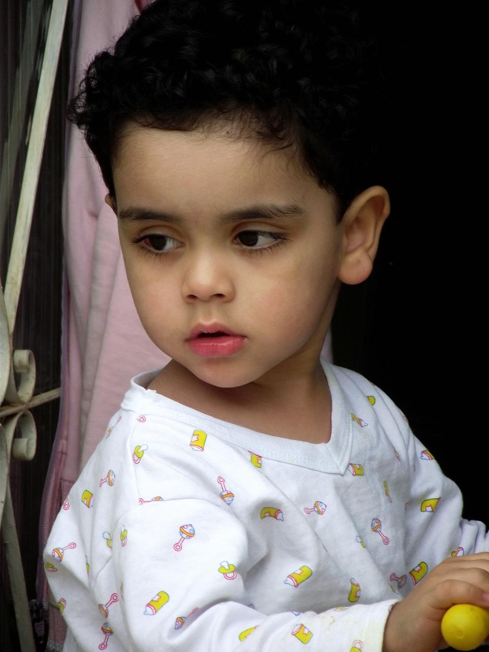 young child holding yellow toy in hand near curtain