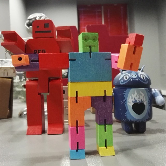 three toy robots are standing around in an office setting