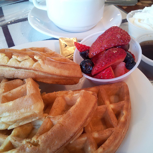 a waffle, fruit and juice sit on a plate
