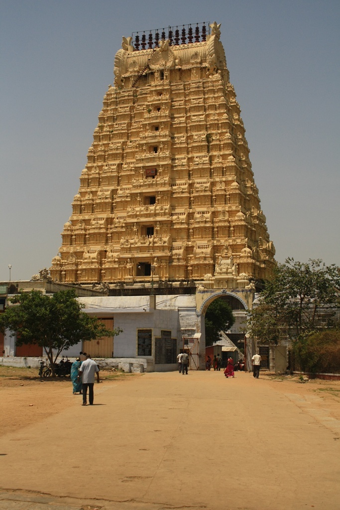 a very tall, elaborate yellow temple structure near people walking