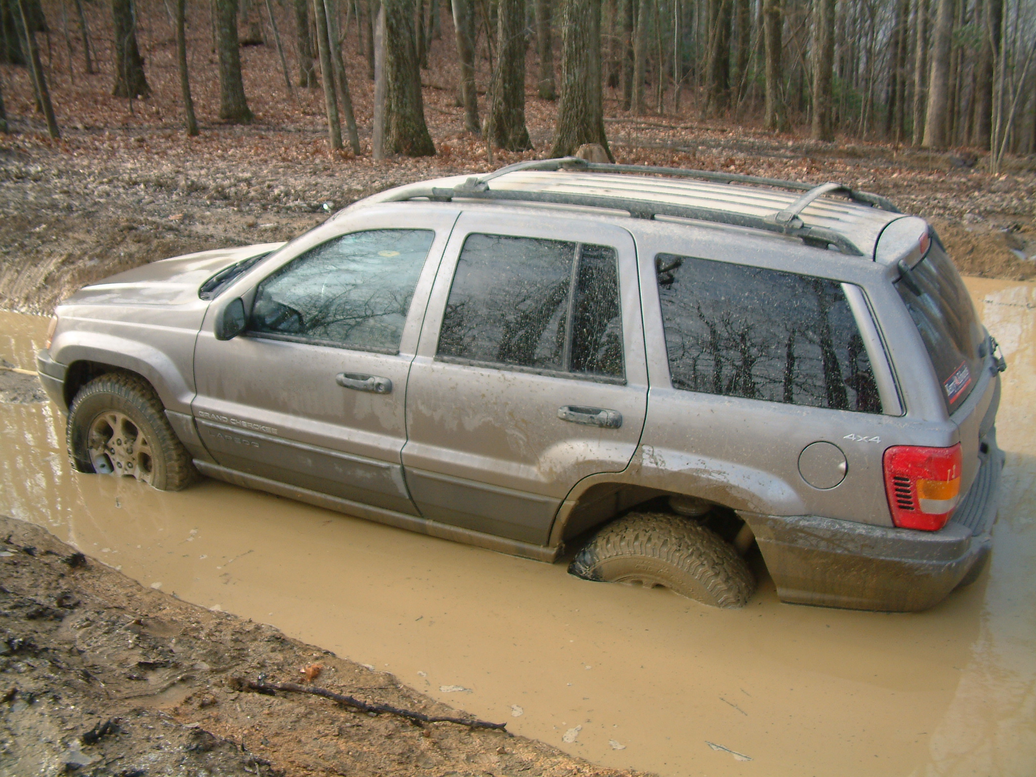 a muddy suv parked in the mud beside trees