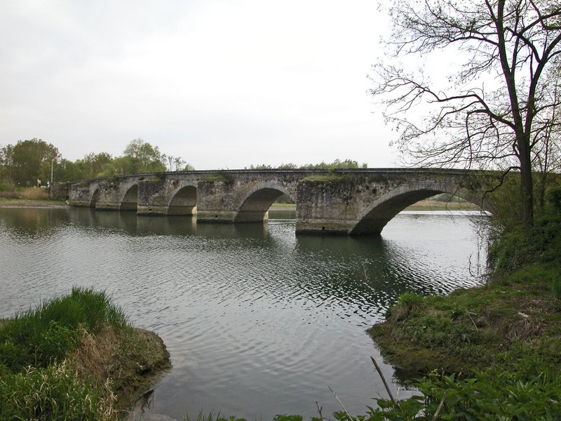 a stone bridge is spanning a river near a green field