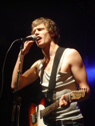 a young man singing into a microphone and playing guitar