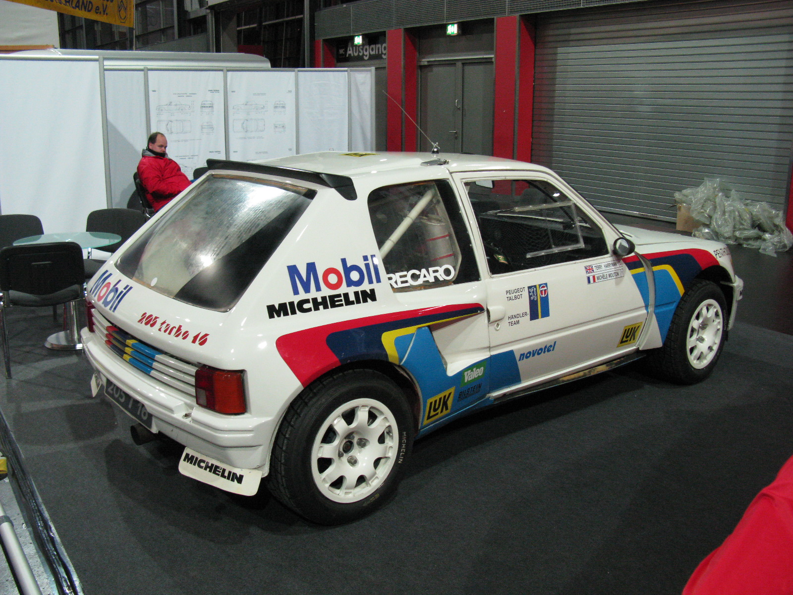 a small car sits in a showroom with workers