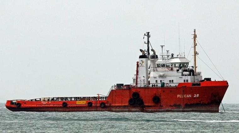 a big orange boat in the water with a large vessel behind it