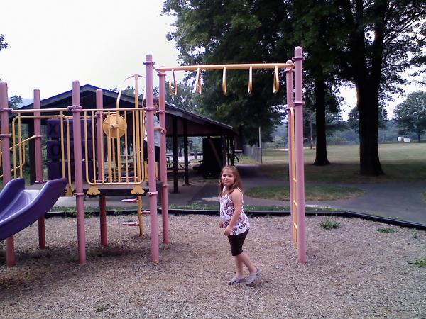 a little girl playing in front of a pink and purple playground set