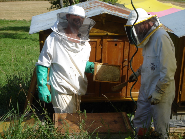 two men in bee suit next to the beehive