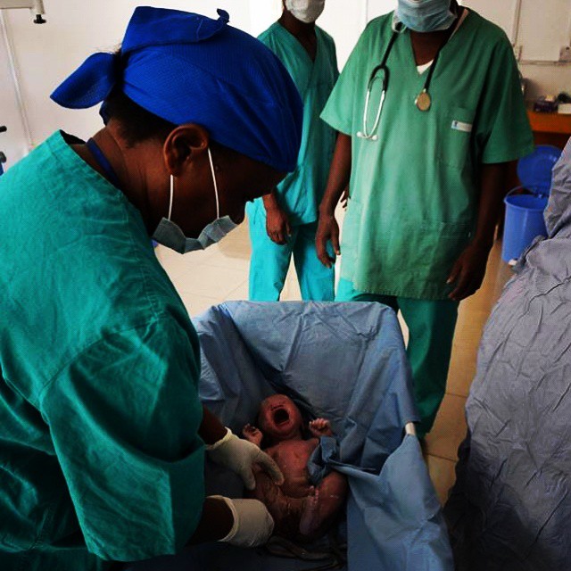 a person wearing surgical gear is looking down on a infant