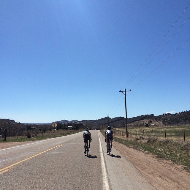 two people on bikes riding down the side of a road