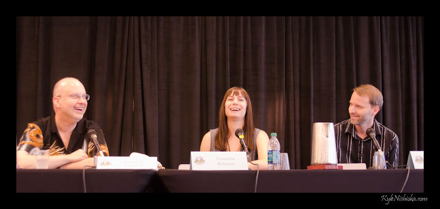 three people are smiling and speaking at a panel
