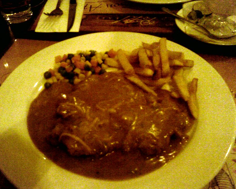 steak and fries with gravy and vegetables on a white plate