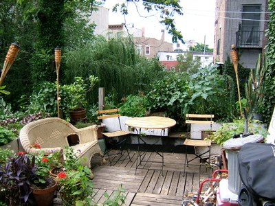 a wooden deck surrounded by green plants next to tall buildings
