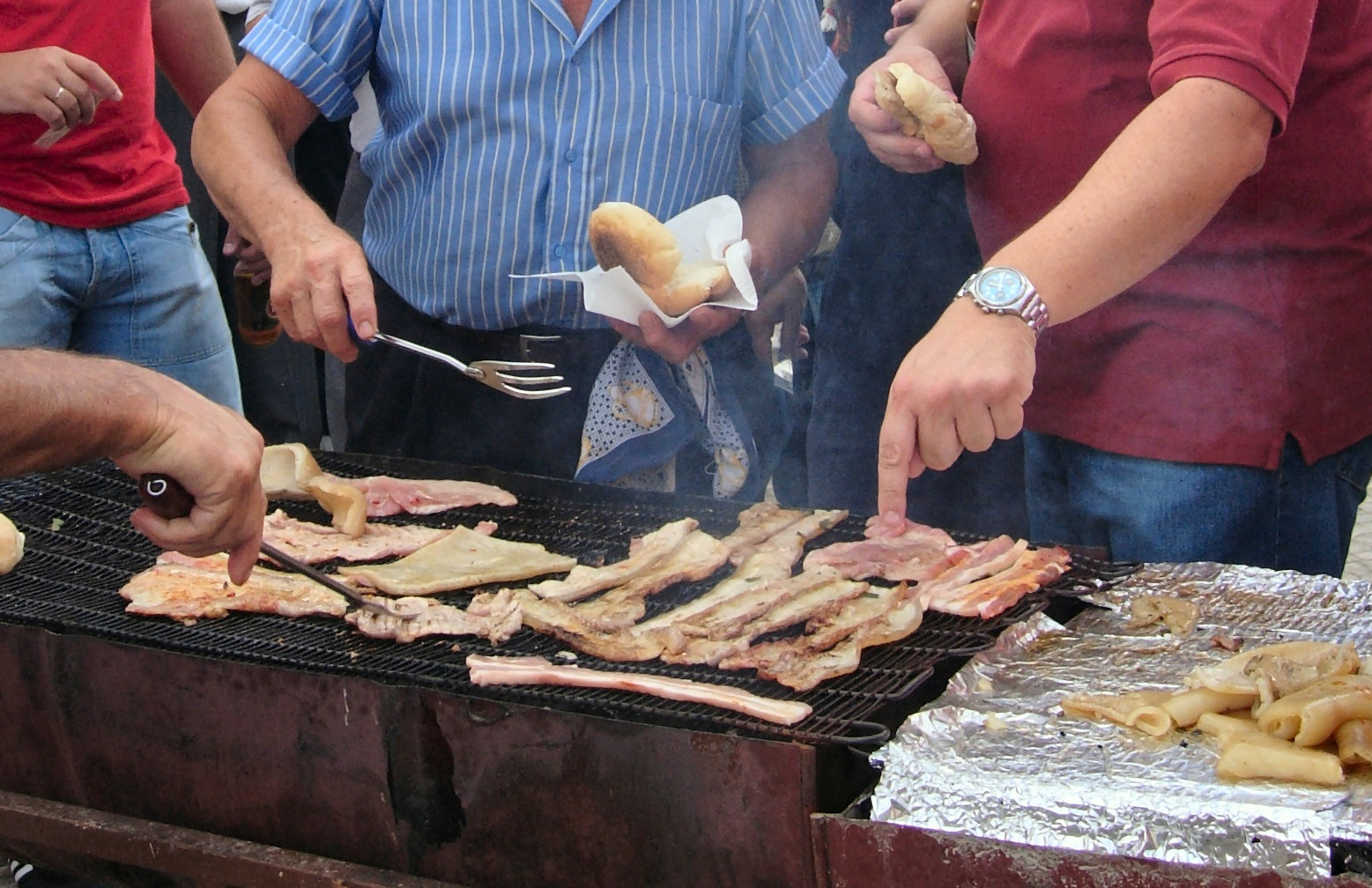 two men standing near a grill getting food on the grill