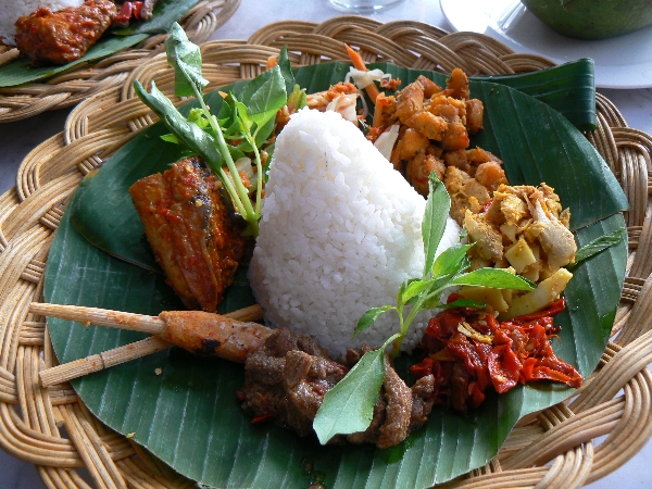 a large plate filled with meat and rice on banana leaves