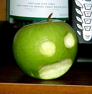 a green apple with a sad face made out of the skin of it