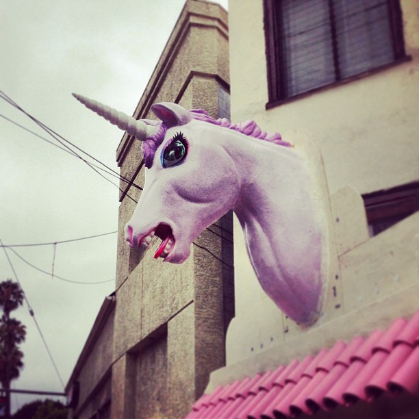 a pink, unicorn - like head hangs over the top of a building