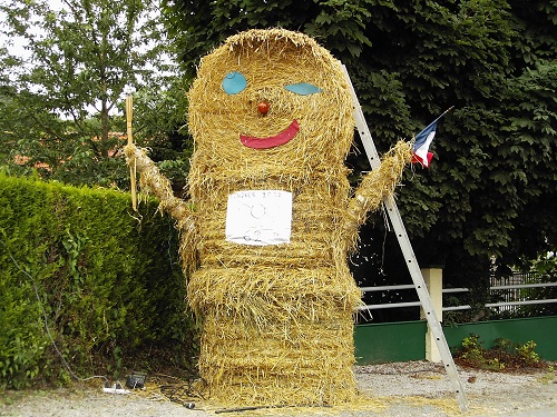 hay scarecrow holding american flag at entrance to parking lot