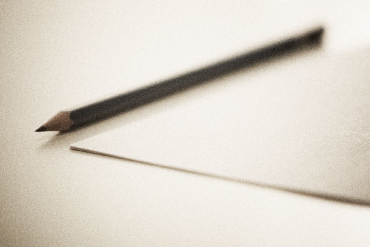 a pencil resting next to a square paper