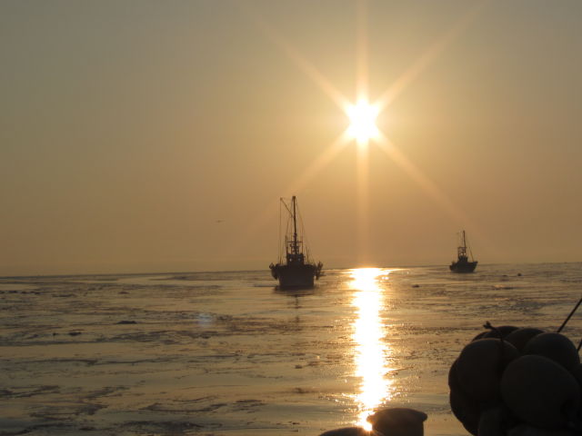 some very small ships on the water and the sun going down