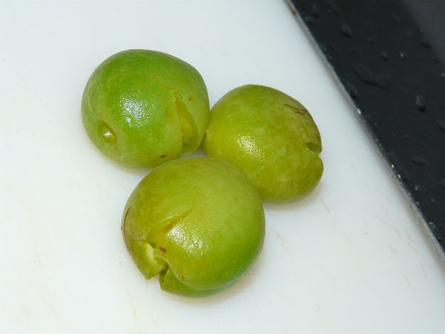 three green fruits are next to a knife on a  board