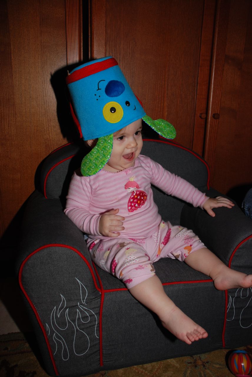 a baby is sitting on a grey chair wearing a cute hat