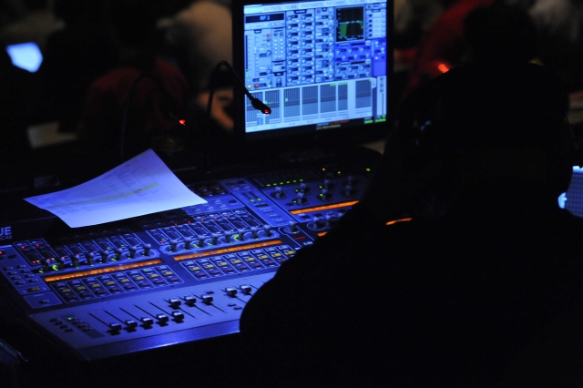 a soundboard, monitor and a set of microphones are illuminated at night
